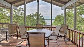 A covered outdoor deck with a table and chairs, overlooking a lake and trees. - 1 Mi to Margaritaville! Cabin w/ Resort Perks (Osage Beach)