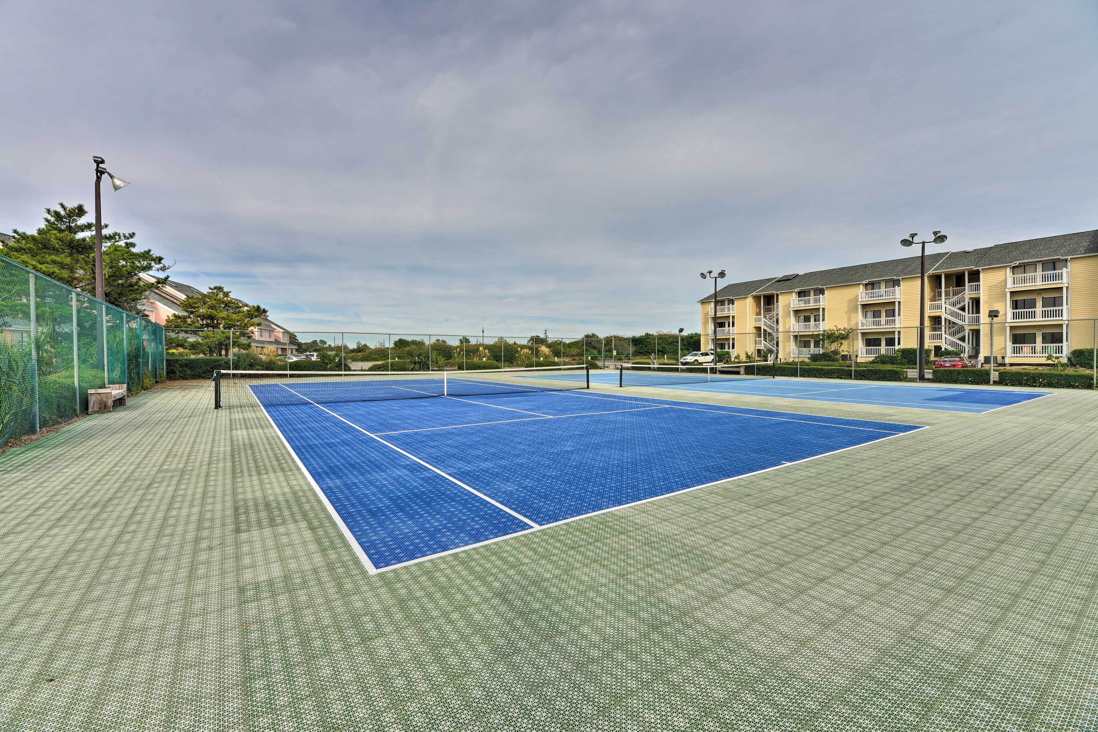 A tennis court with a net, surrounded by a fence and a building with multiple balconies.