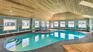 Una piscina interior con techo de madera, ventanas amplias y una zona de estar con sillones.