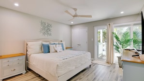 Un dormitorio con cama, mesita de noche, ventilador de techo y vista al exterior.