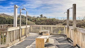 Una terraza de madera con un banco y una mesa, rodeada por una cerca de madera y vegetación.