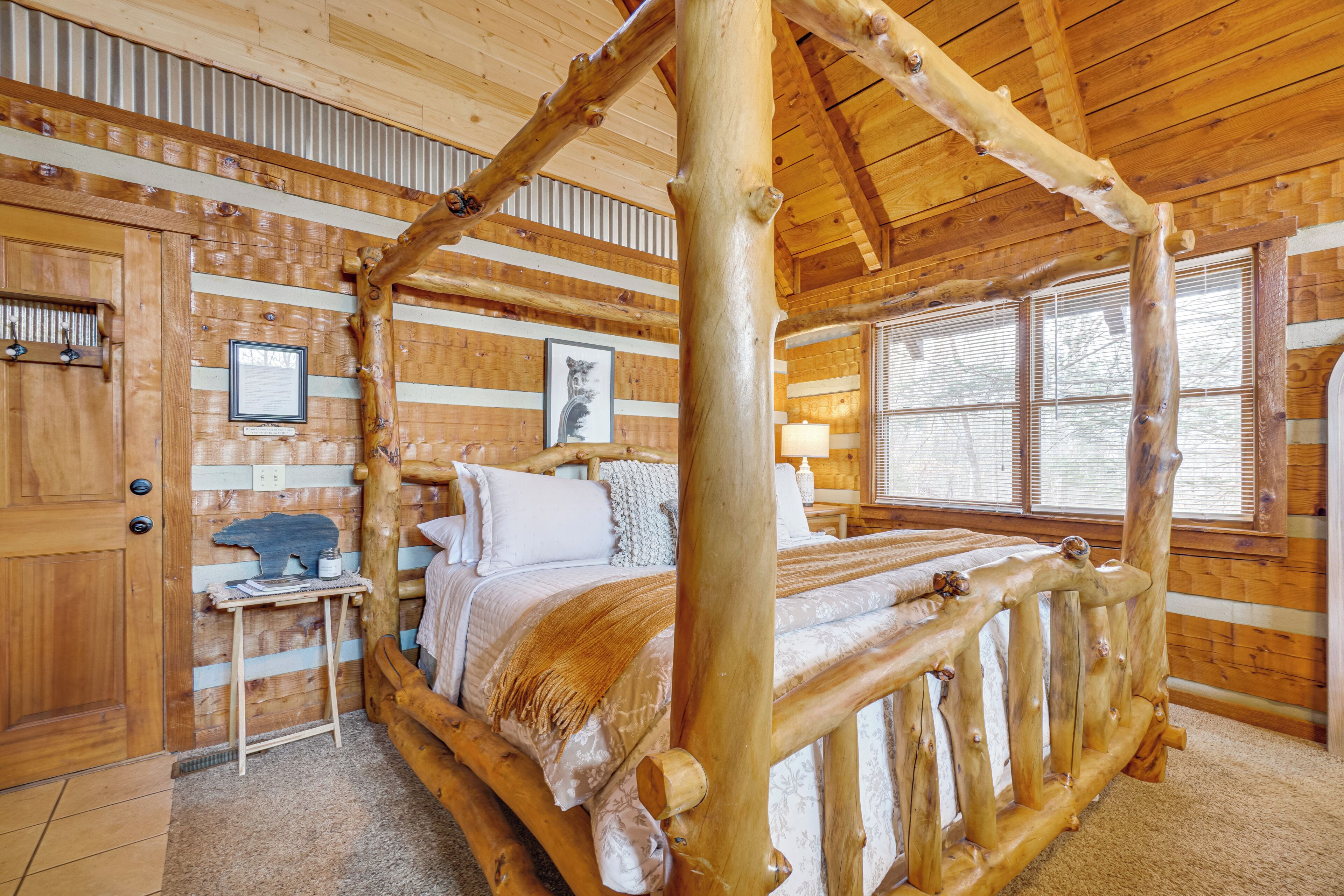 A log cabin room with a four-poster bed, wooden walls, and a window with blinds.