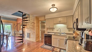 A modern kitchen with a built-in dishwasher, stainless steel appliances, and a spiral staircase leading to a loft bedroom.