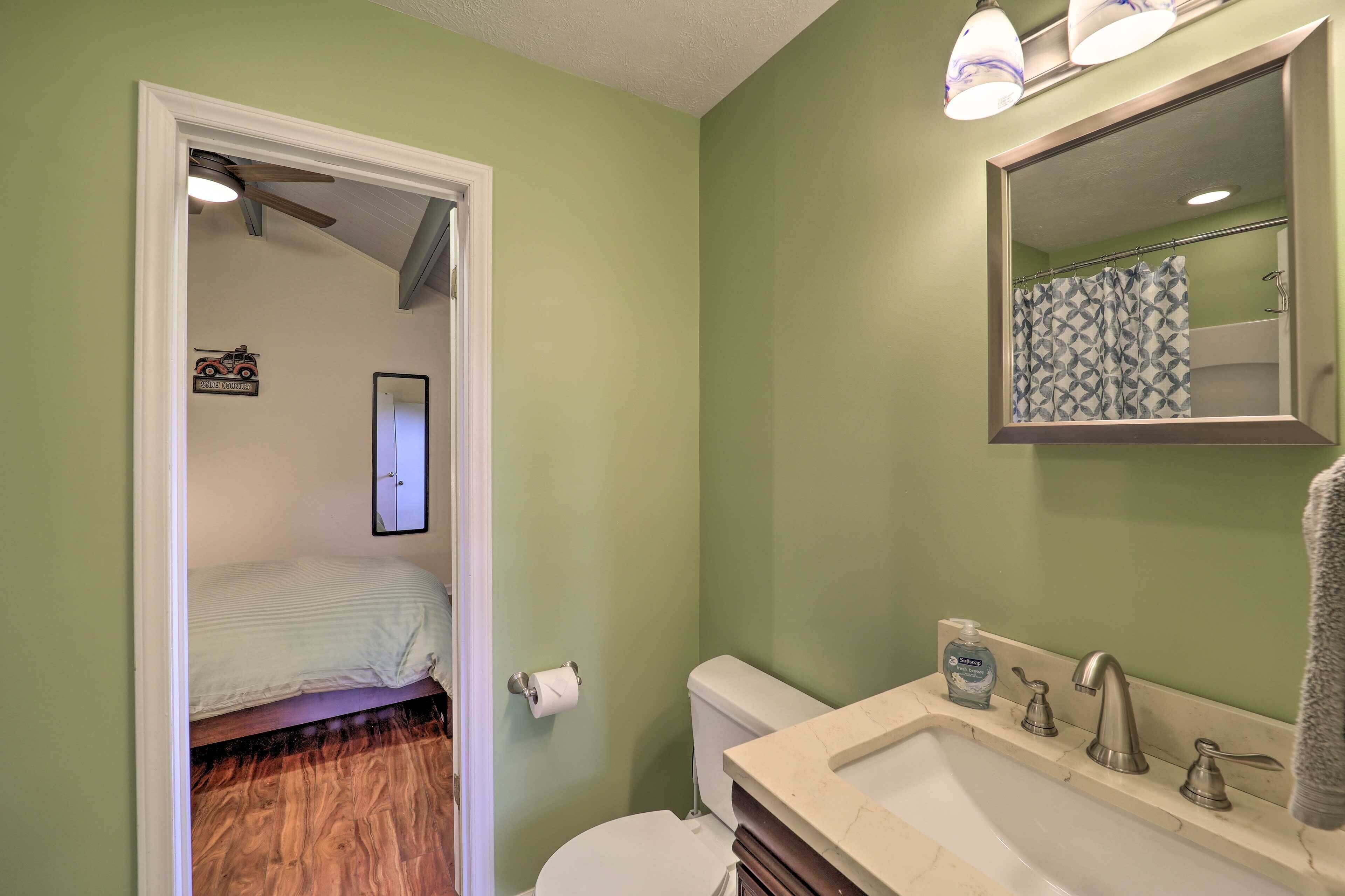 A bathroom with a green wall, a white toilet, a sink with a mirror, and a shower curtain.
