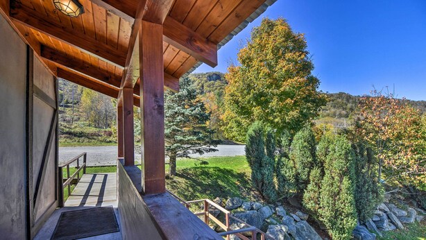 A wooden covered porch with a view of a mountainous landscape and a road.