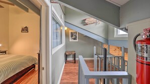A bedroom with a bed, a small table, and a window. There is a staircase leading to an upper level with a railing.