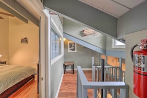 Un dormitorio con una cama, una mesita y una ventana. Se ve una escalera que sube a un nivel superior, con barandilla.