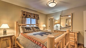 A cozy bedroom with a wooden bed frame, a large window with curtains, two bedside lamps, and a mirror on the wall. - Cabin w/ Hot Tub: 3 Mi to Main St Breckenridge! (Breckenridge)
