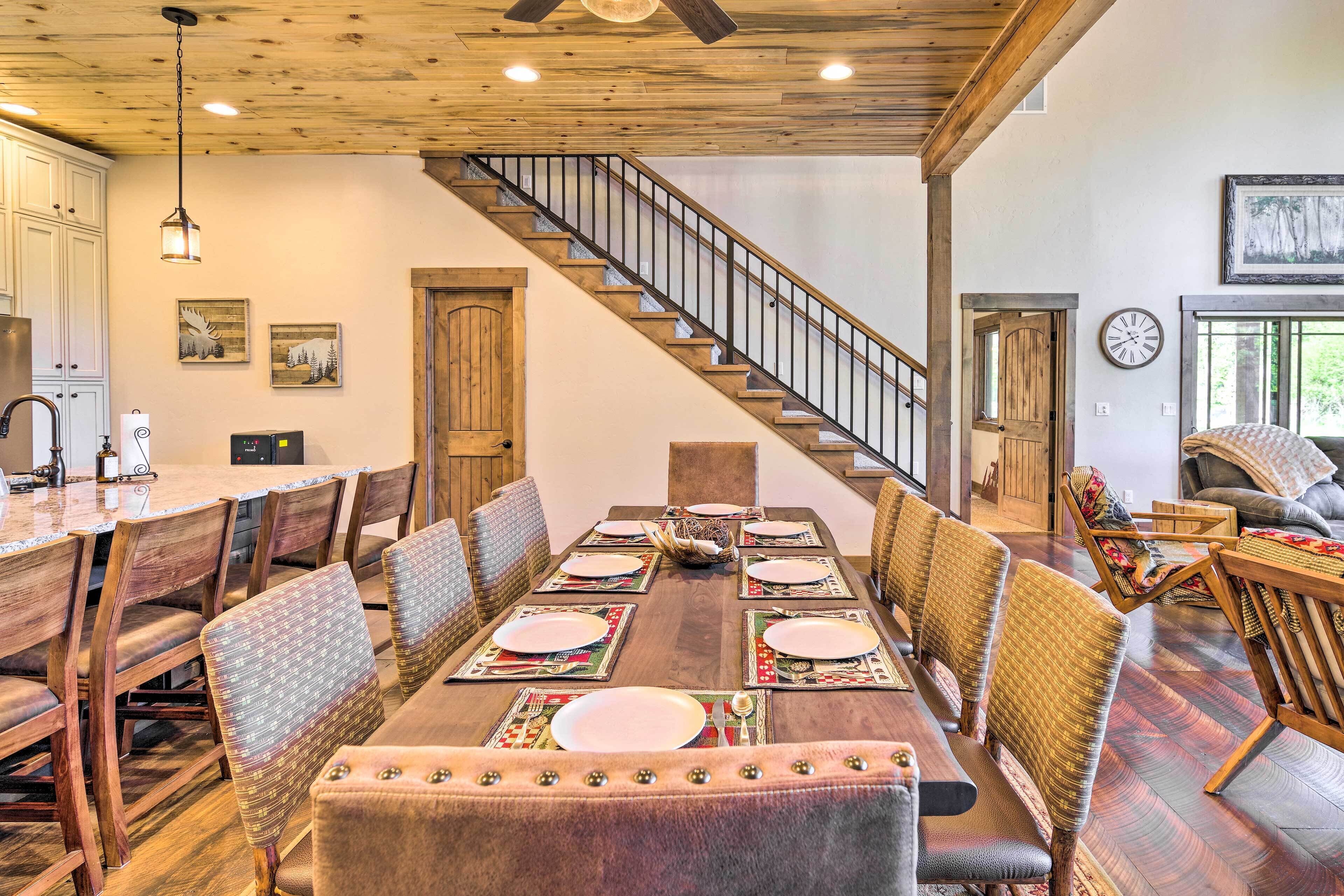 Un espace repas avec une table en bois dressée pour six personnes, entourée de chaises rembourrées. Un escalier avec une rampe en bois mène à un autre niveau.