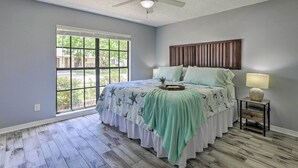 Un dormitorio con cama, mesita de noche, ventilador de techo y ventana con vistas.