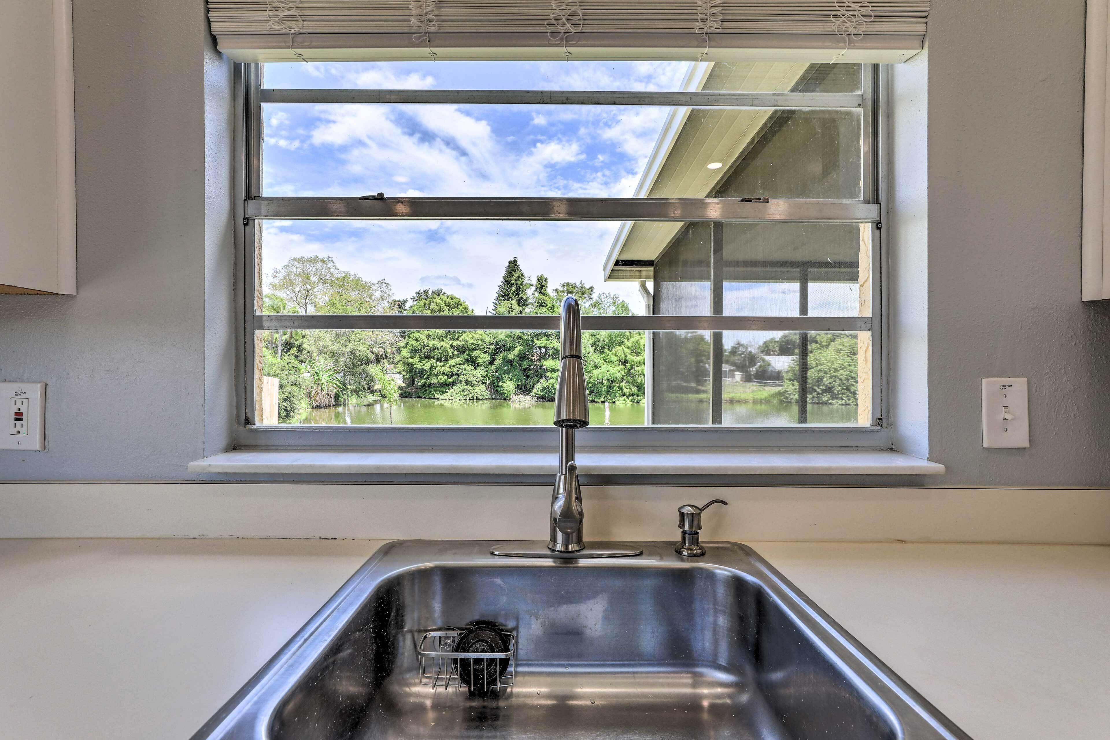 A kitchen with a stainless steel sink, a window with a view of greenery, and a white countertop.