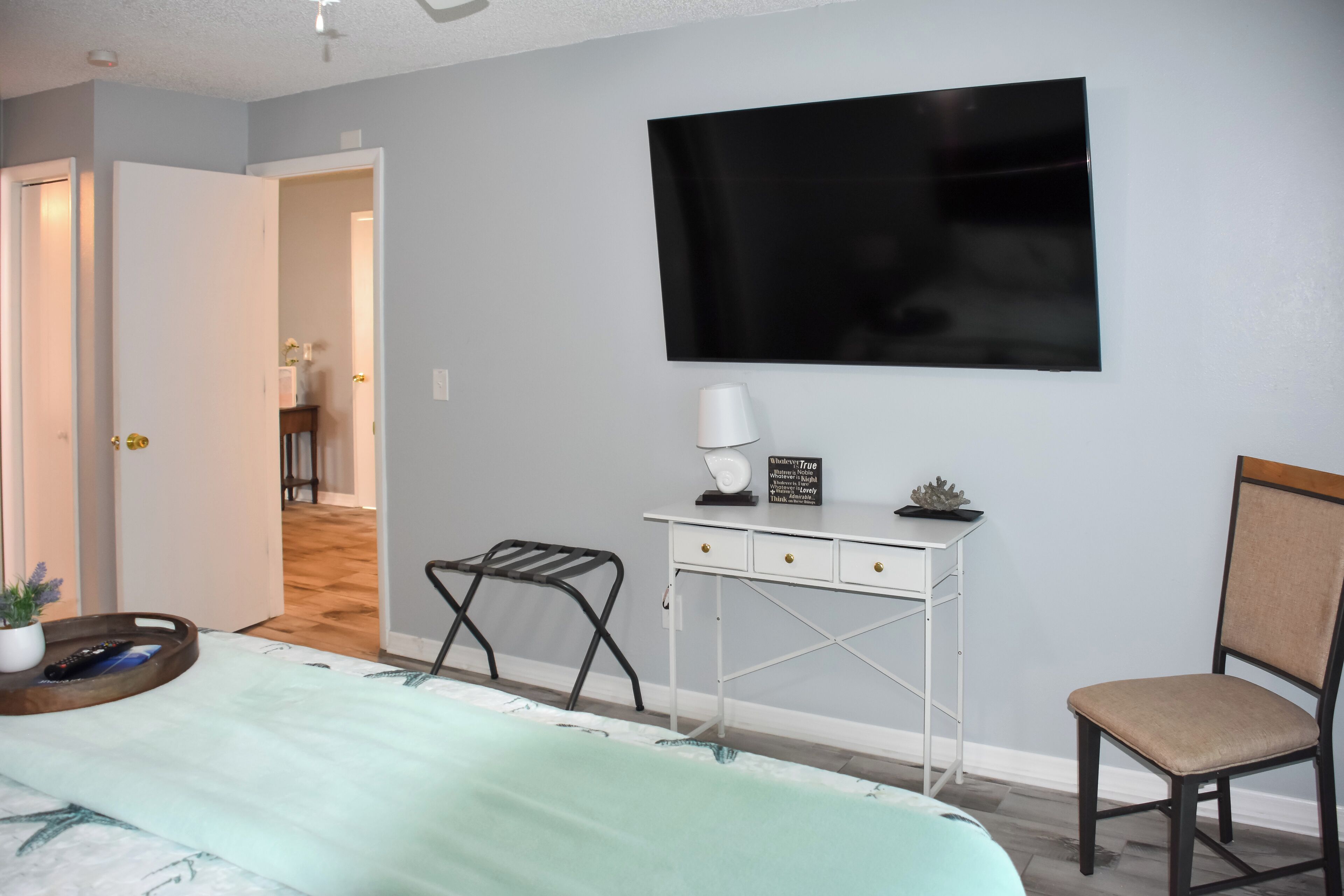 Une chambre à coucher comprenant un lit, un bureau, une chaise, un téléviseur et une porte donnant sur une autre pièce.