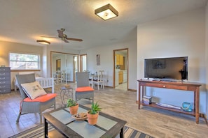 A spacious living room with a ceiling fan, a television on a wooden stand, and a dining area in the background. - Bayfront Panama City Studio Near Tyndall Afb! (Panama City)