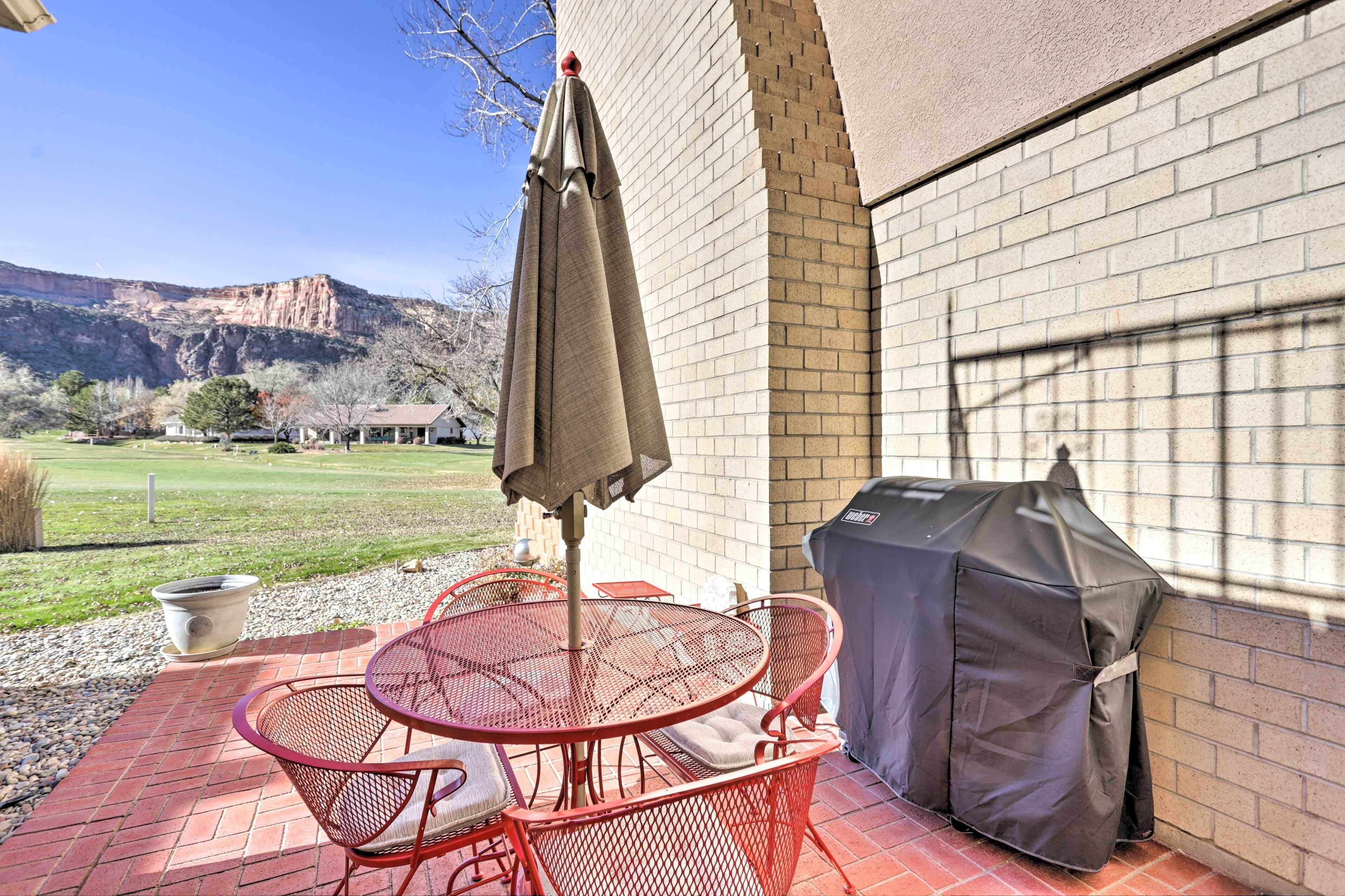Un patio con una mesa redonda y sillas, una parrilla y vistas a la montaña.