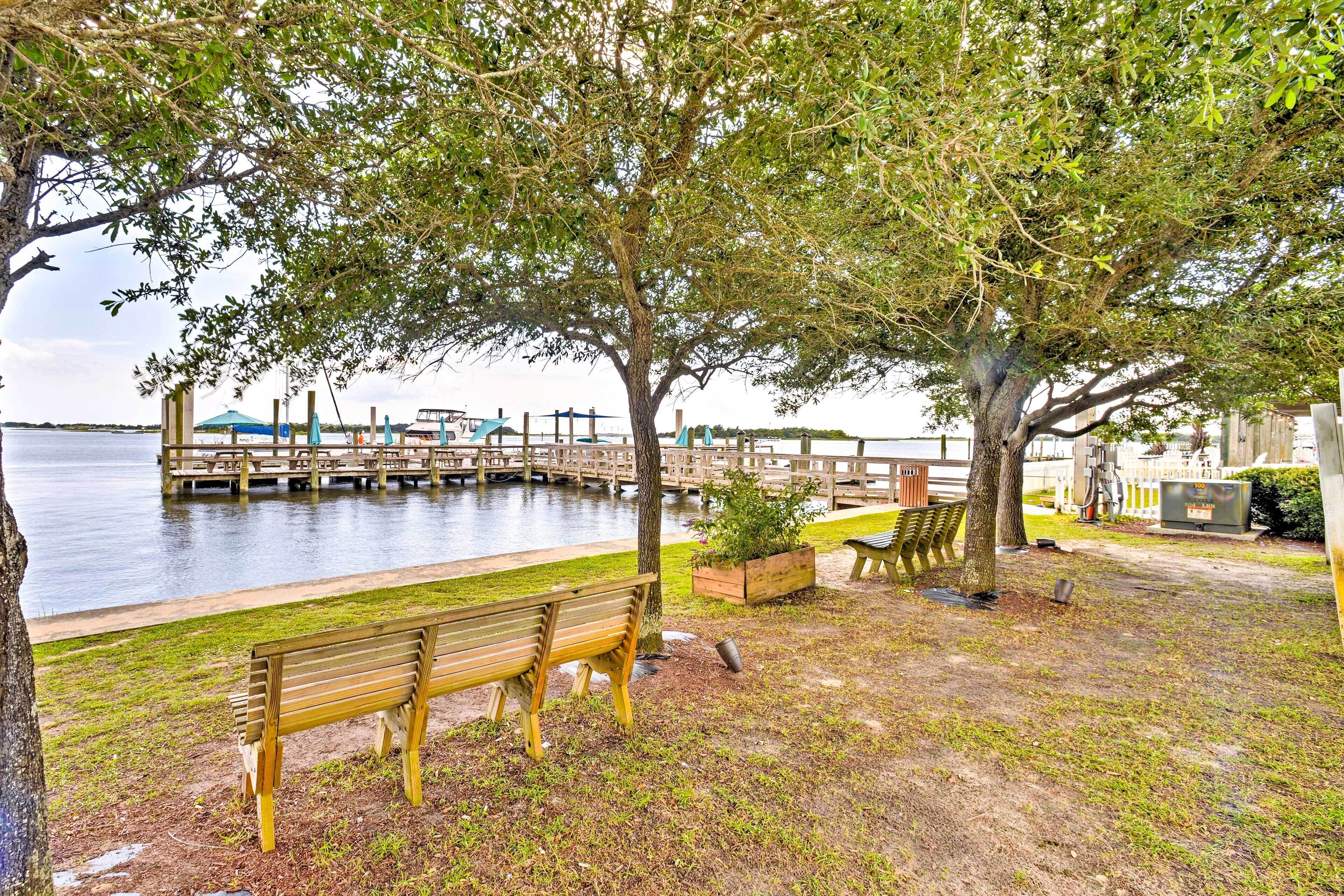 A waterfront park with a wooden bench, picnic tables, and a dock extending into the water.