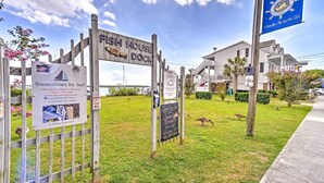 A wooden sign for Fish House Dock, a sailing charter service, with a grassy area and a building in the background. - Historic Swansboro Studio w/ Intracoastal View! (Swansboro)