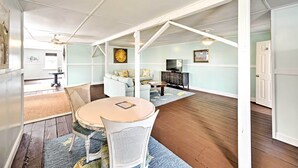 A dining area with a round table and chairs, a sofa, and a television in a room with wooden floors and light blue walls. - Historic Swansboro Studio w/ Intracoastal View! (Swansboro)