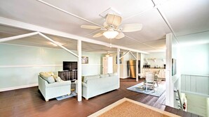 A spacious living area with a high ceiling fan, a sofa, a television, and a kitchen in the background. - Historic Swansboro Studio w/ Intracoastal View! (Swansboro)