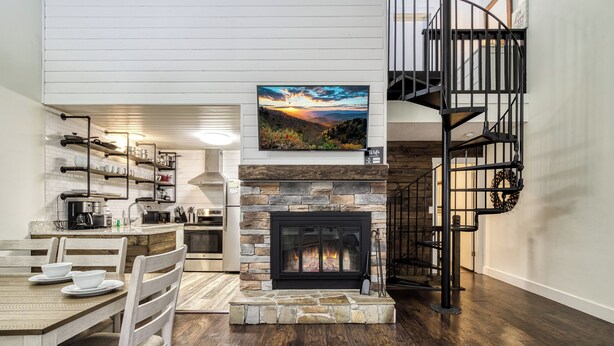 A modern kitchen with white cabinets, a stone fireplace, and a dining area with a wooden table and chairs. - Walkable Dtwn Gatlinburg Townhome w/ Pool Access! (Gatlinburg)