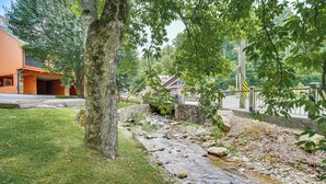 A stone stream with a tree on the left, a building with orange walls, and a fence with a yellow sign in the background. - Walkable Dtwn Gatlinburg Townhome w/ Pool Access! (Gatlinburg)