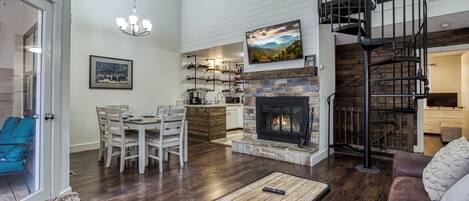 A spacious living area with a fireplace, dining table, and comfortable seating. A spiral staircase leads to an upper level.