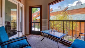 A balcony with a glass table and chairs, a door leading outside, and a view of a brick building. - Walkable Dtwn Gatlinburg Townhome w/ Pool Access! (Gatlinburg)