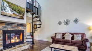 A modern living room with a fireplace, a brown leather sofa, a coffee table, and a spiral staircase. - Walkable Dtwn Gatlinburg Townhome w/ Pool Access! (Gatlinburg)