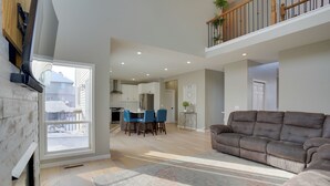 A spacious living room with a large brown sofa, a dining area with blue chairs, and a kitchen in the background. - Cozy Eden Prairie Home < 21 Mi to Twin Cities (Eden Prairie)