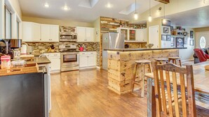 A modern kitchen with white cabinets, stainless steel appliances, and a wooden island with stools. - Troutfest: Anglers Retreat on White River w/ Deck (Cotter)