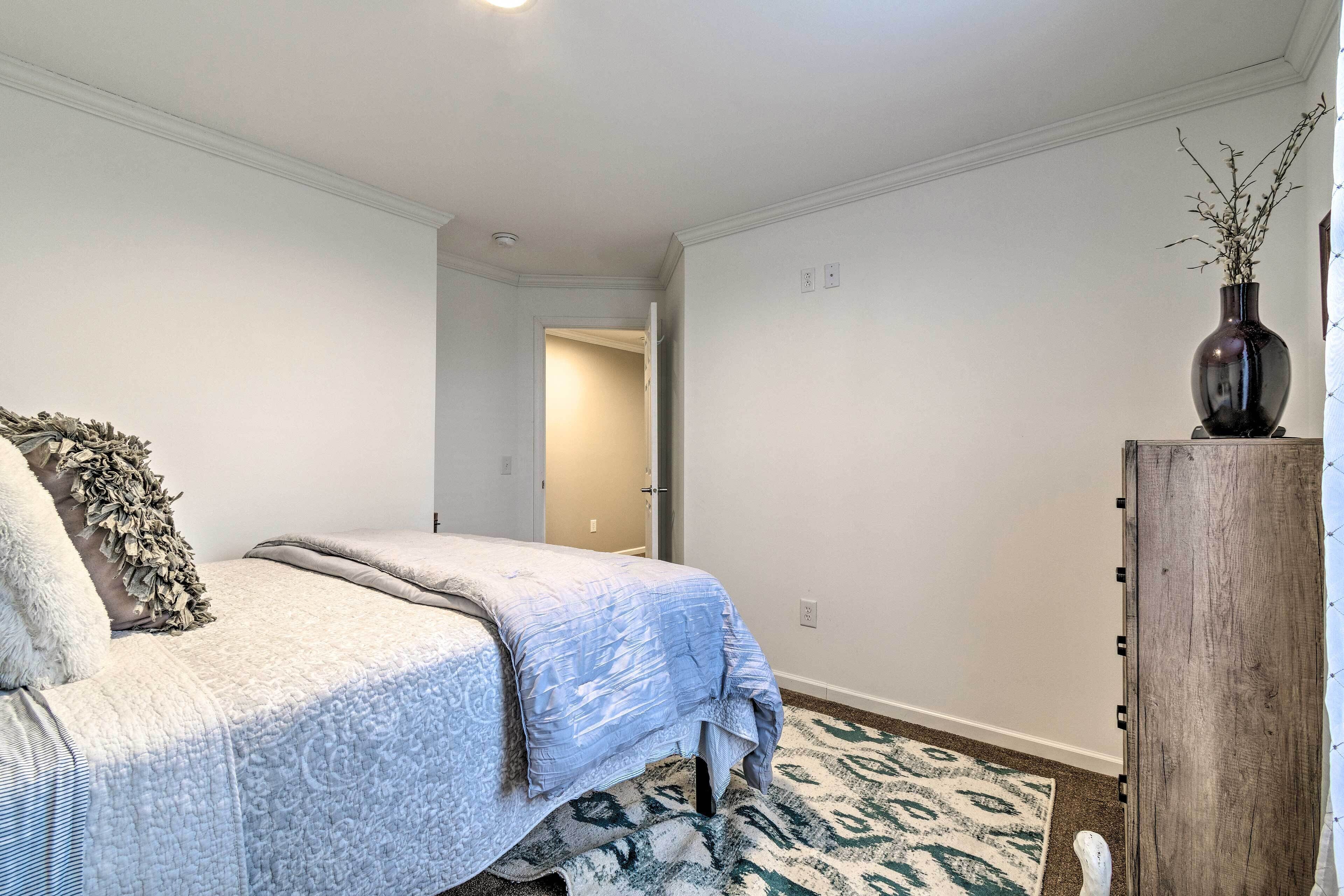 A bedroom with a bed, a wooden nightstand, a vase with branches, and a patterned rug.