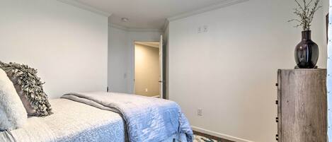 A bedroom with a bed, a wooden nightstand, a vase with branches, and a patterned rug.