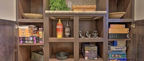 A wooden cabinet with shelves containing board games, a bottle, and decorative items.