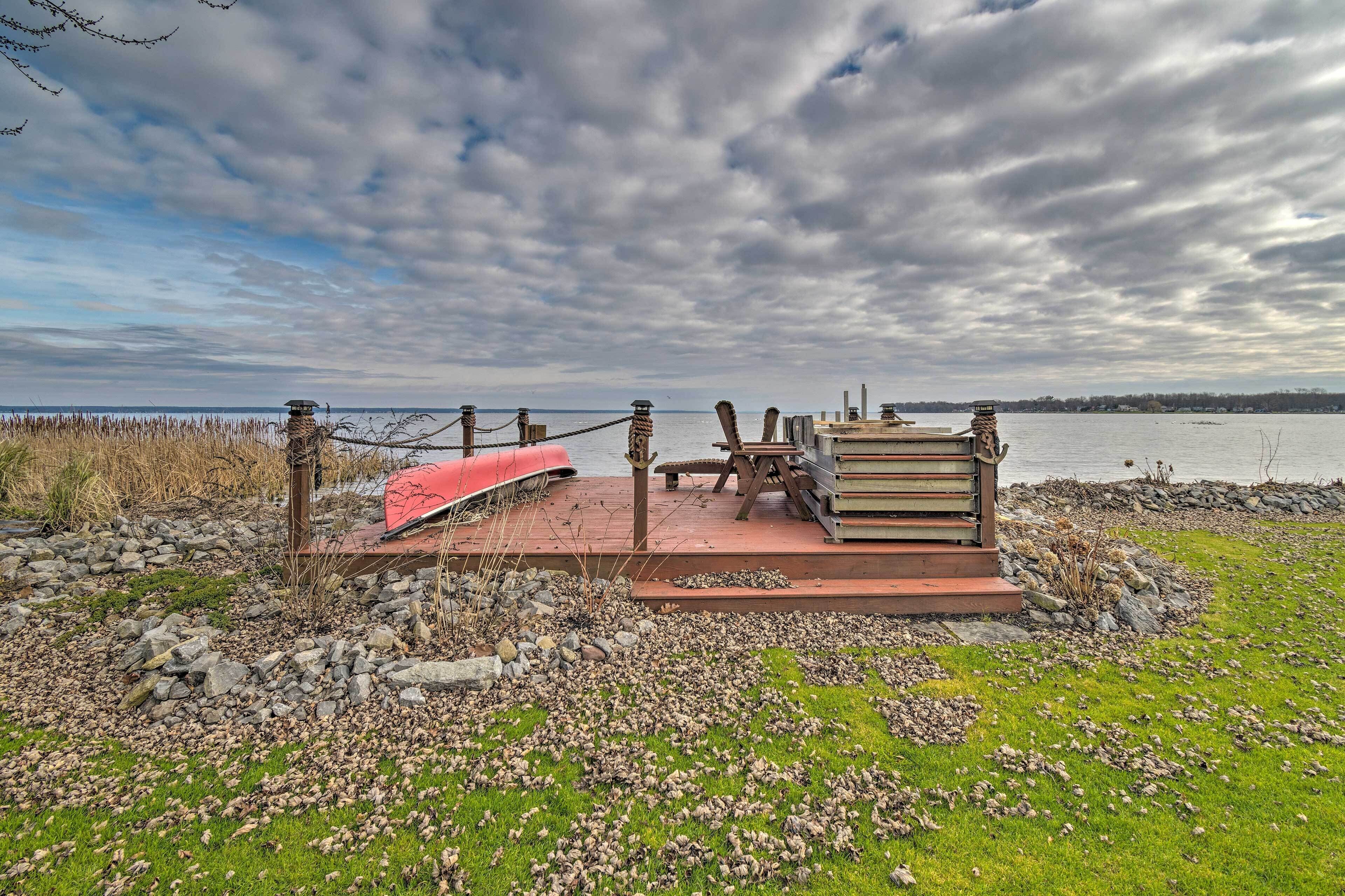 Um deck à beira do lago com um canoa vermelha, mesa de piquenique e uma pilha de livros.