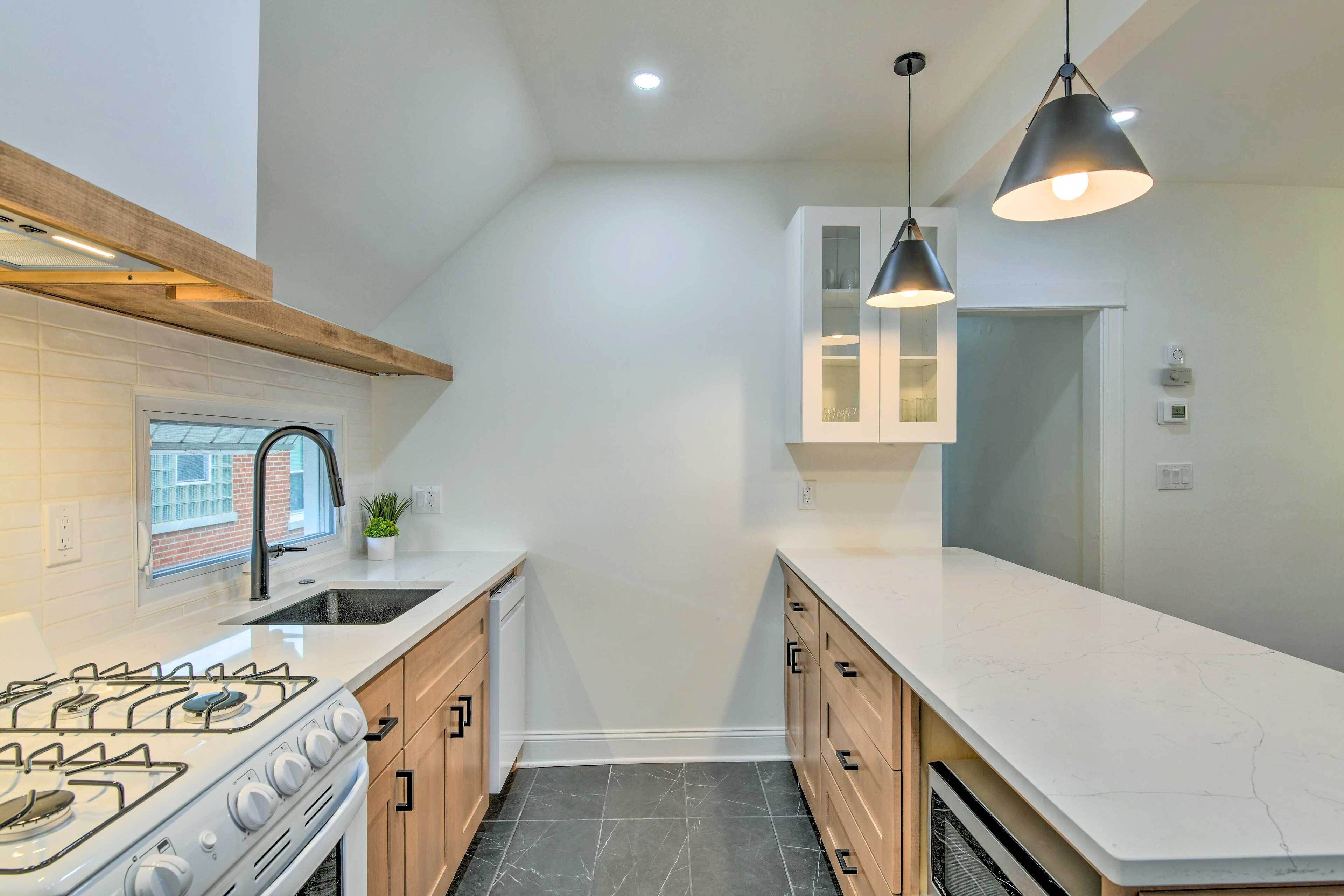 Une cuisine moderne dotée d’une cuisinière à gaz, de meubles blancs et de luminaires suspendus.