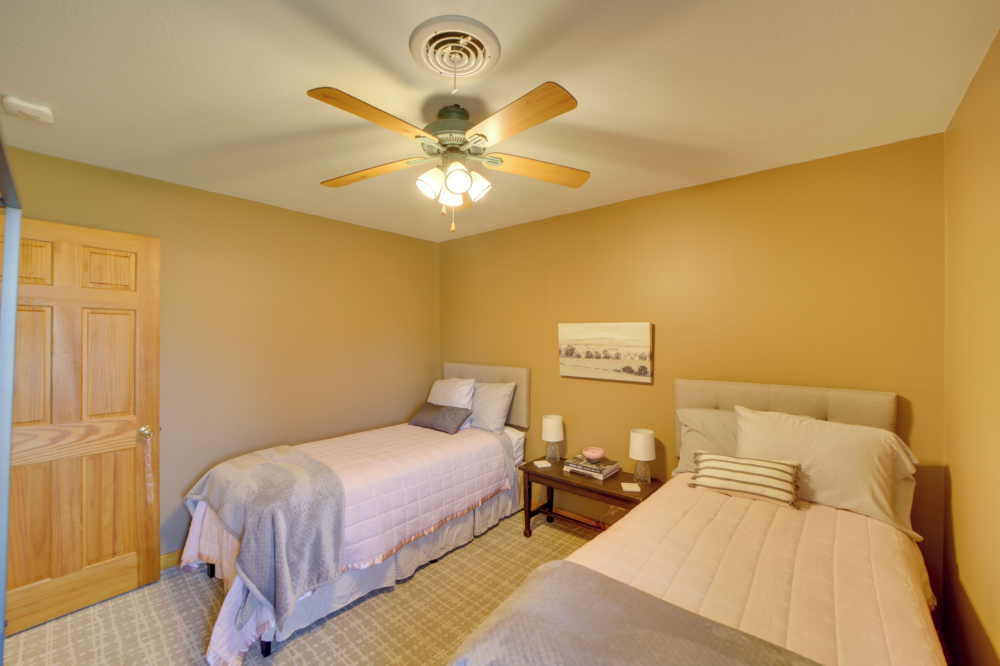 A bedroom with two beds, a ceiling fan, a nightstand with lamps, and a door.