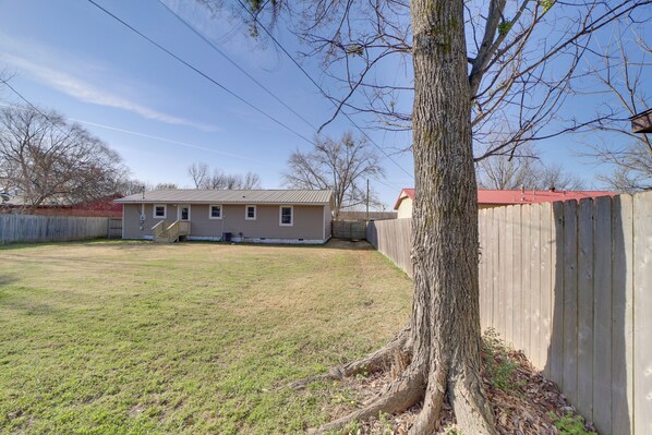 A backyard with a wooden fence, a tree, and a house with a red roof.