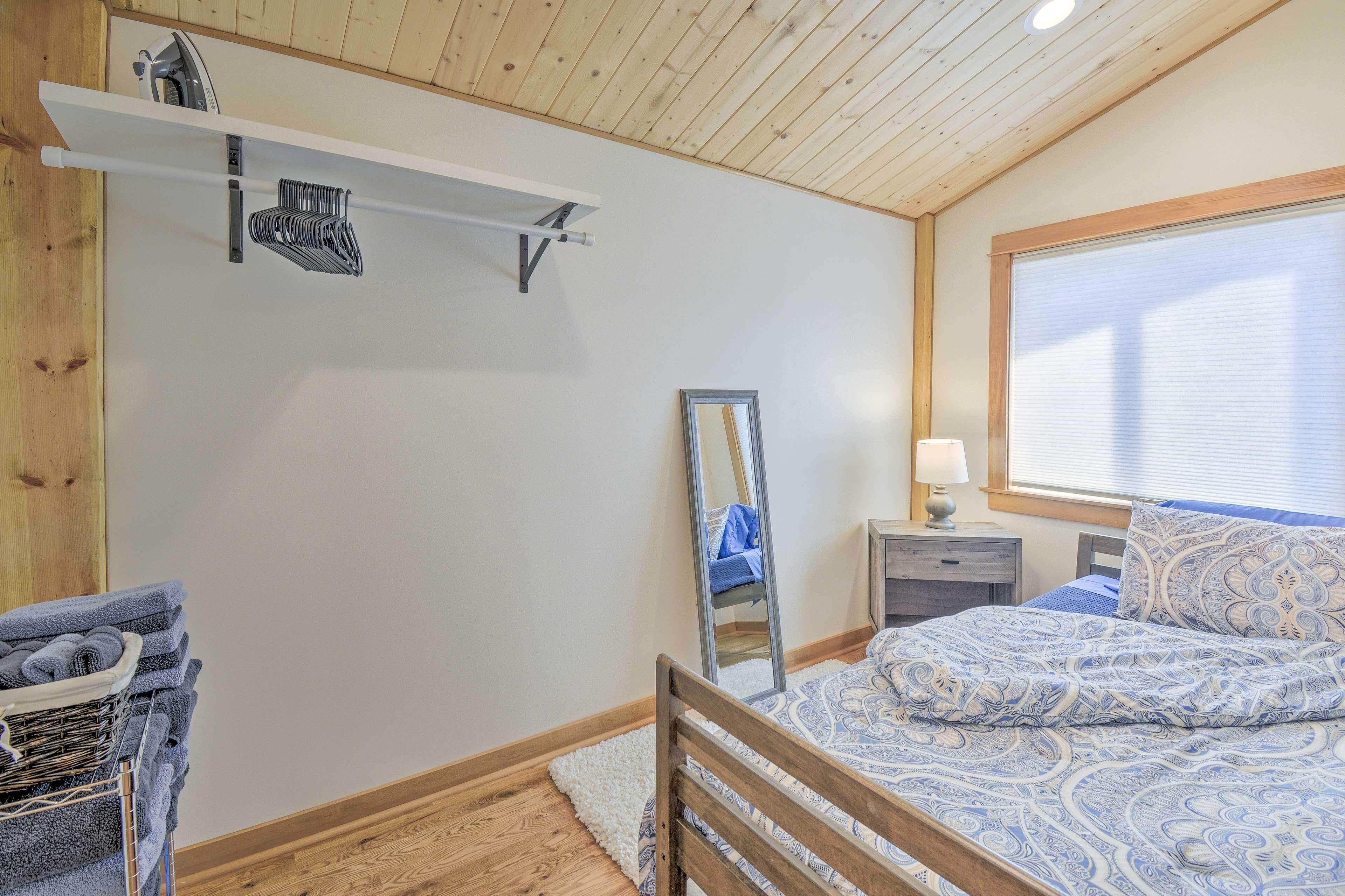 Une chambre avec un plafond en bois, un lit avec une literie à motifs, une table de chevet avec une lampe, un miroir et une étagère murale avec des serviettes.