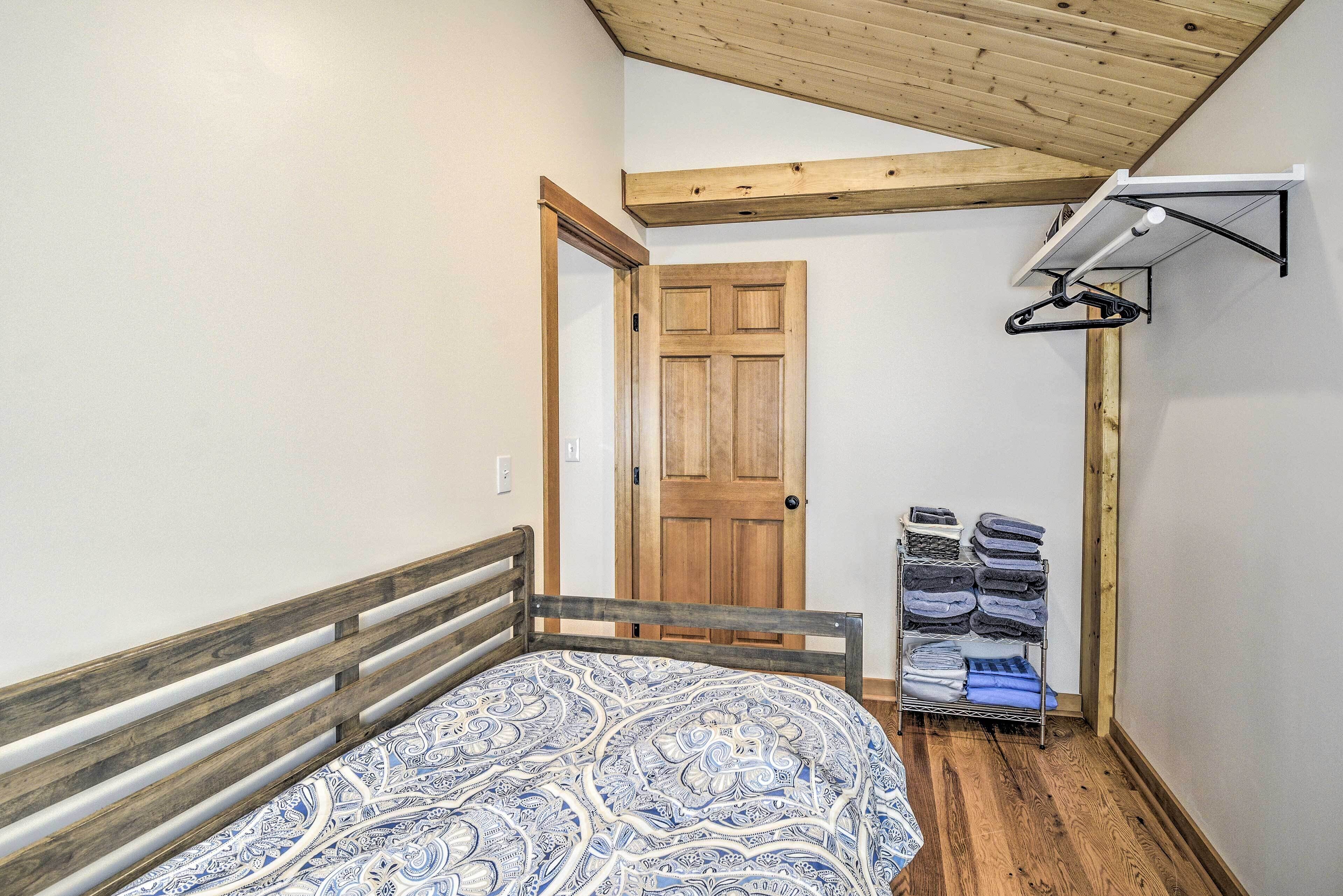 A bedroom with a wooden bed frame, a patterned bedspread, a wooden door, and a wall-mounted drying rack.