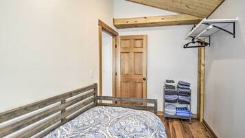 A bedroom with a wooden bed frame, a patterned bedspread, a wooden door, and a wall-mounted drying rack.