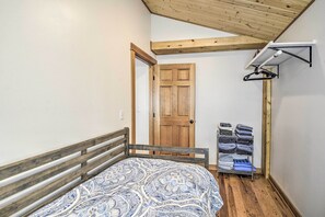 Une chambre avec un lit en bois, une couvre-lit à motifs, une porte en bois et un étendoir fixé au mur.