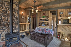 A cozy cabin interior with a stone wall, a fireplace, a leather couch, a wooden bar, and a ceiling fan.