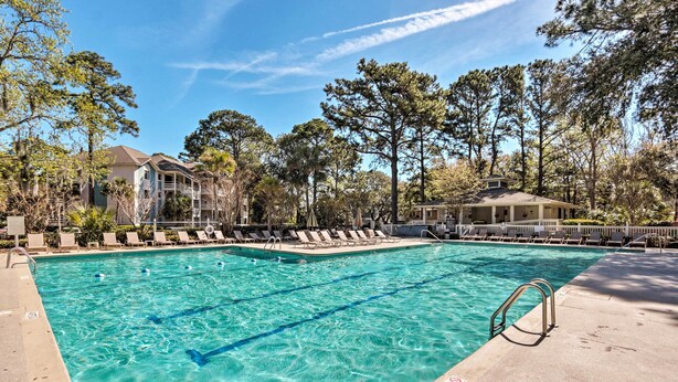 A swimming pool with clear water, surrounded by lounge chairs and trees.