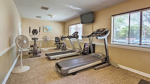 A fitness room with treadmills, elliptical machines, and a fan.
