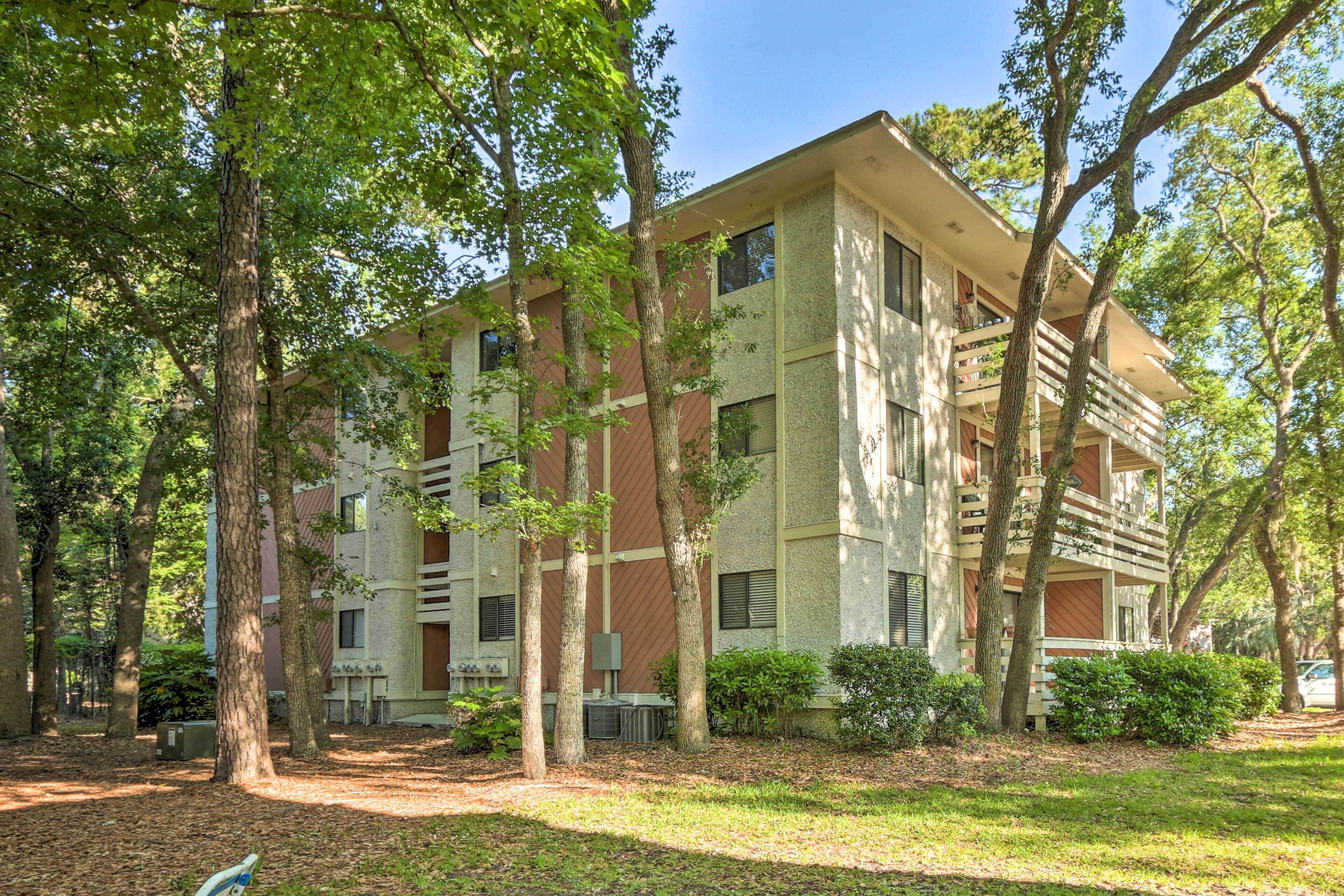 A multi-story building with a modern architectural style, surrounded by trees and a grassy area.