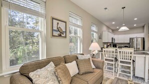 A living room with a brown sofa, patterned cushions, and a large window with blinds. - Modern Escape in the Heart of Murrells Inlet (Murrells Inlet)