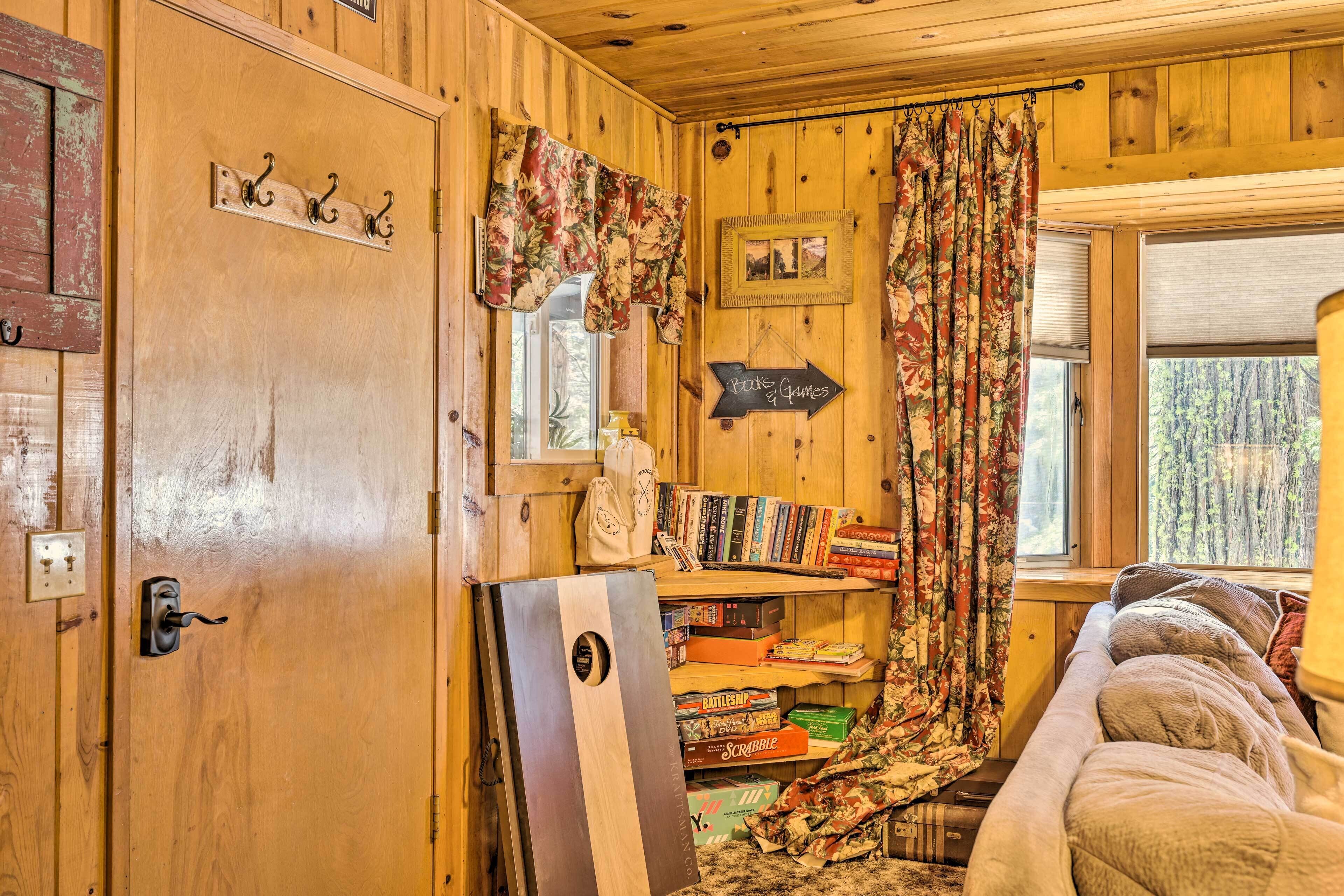 A cozy room with wooden walls, a bed, a bookshelf with games, and a window with curtains.