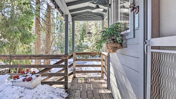 A covered porch with a wooden bench, a planter with plants, and a snow-covered ground. - California Retreat w/ Deck, Fire Pit & Grill! (Long Barn)
