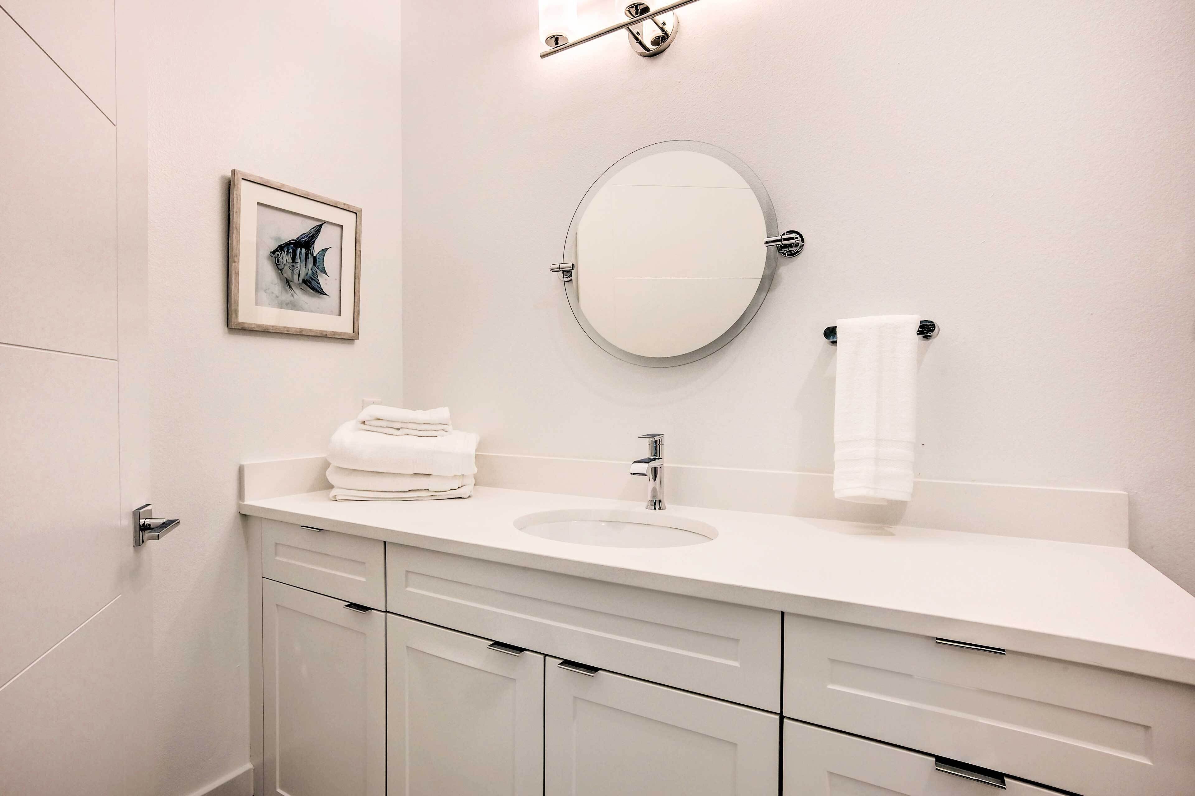 A modern bathroom with a white sink, a round mirror, and a framed picture on the wall.