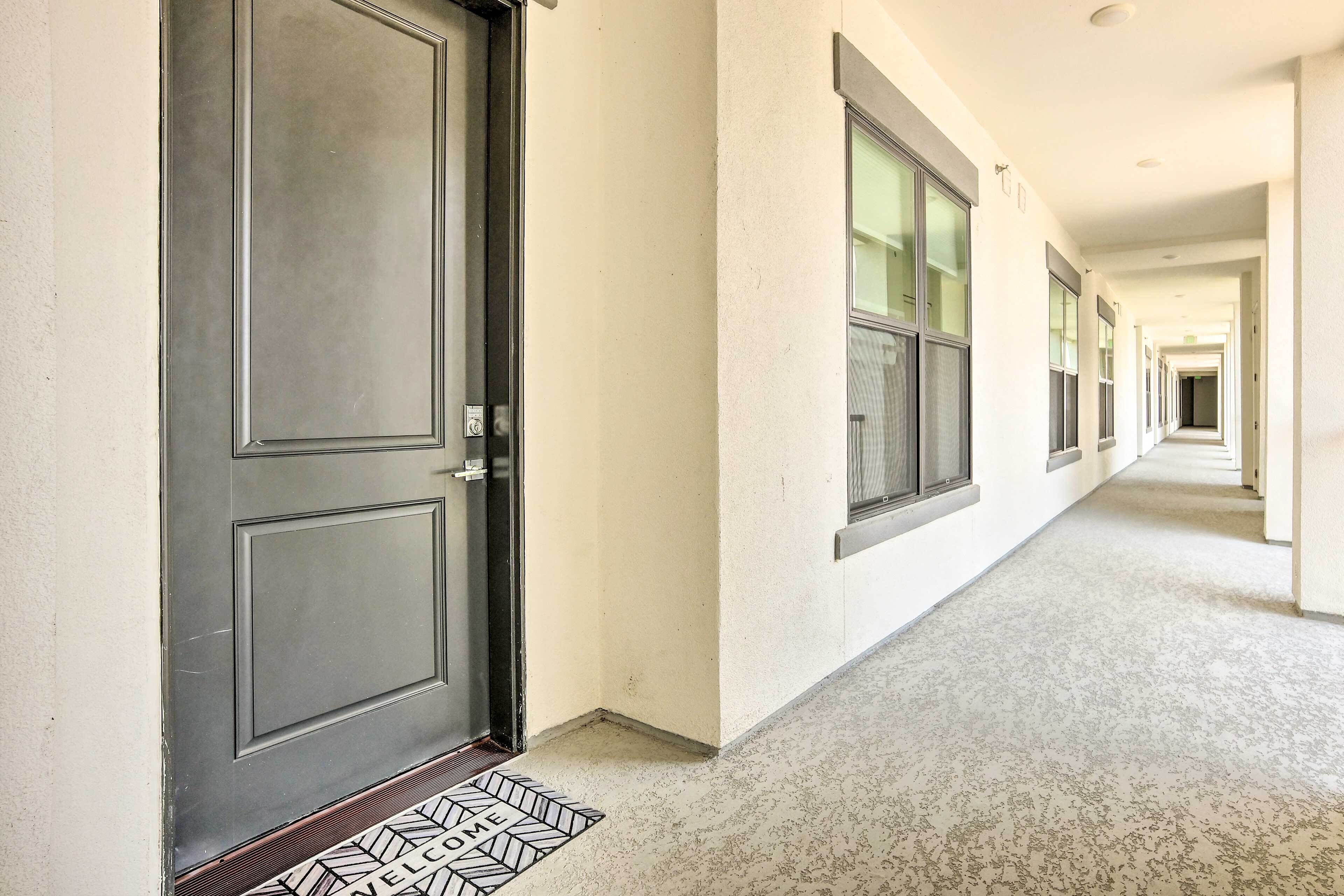 A hotel corridor with a closed door, a welcome mat, and a long hallway with windows and doors.
