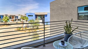 En balkon med udsigt over moderne bygninger, en potteplante og udendørs møbler.
